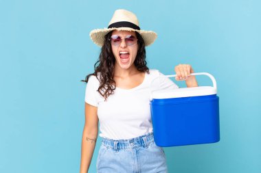 Güzel İspanyol bir kadın agresif bir şekilde bağırıyor. Elinde taşınabilir bir buzdolabı tutarken çok kızgın görünüyor.