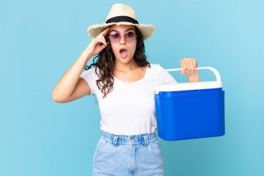 Güzel İspanyol bir kadın şaşırmış görünüyor, yeni bir düşünce, fikir ya da konsept olarak taşınabilir bir buzdolabı tutuyor.