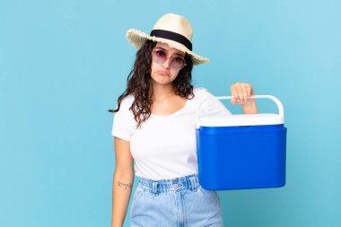 Güzel İspanyol bir kadın üzgün ve sızlanıyor. Mutsuz bir bakışı var ve elinde portatif bir buzdolabı tutarak ağlıyor.