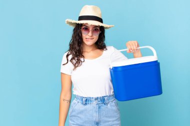 Güzel İspanyol kadın kafası karışmış ve elinde taşınabilir bir buzdolabı tutuyor.