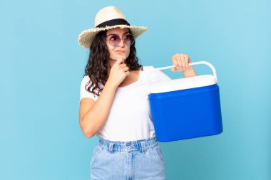 Düşünen, kuşkulu ve kafası karışmış İspanyol bir kadın portatif bir buzdolabı tutuyor.