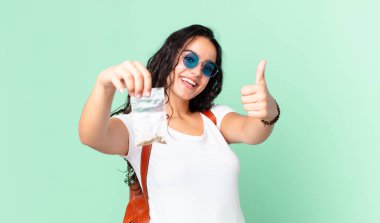 İspanyol güzel kadın gururlu, olumlu gülümsüyor başparmakları havada ve elinde bir marihuana çantası var.
