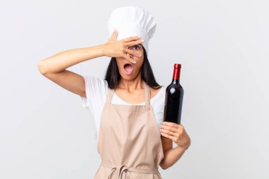 Güzel İspanyol aşçı kadın şok olmuş, korkmuş ya da korkmuş görünüyor. Yüzü elle kaplanmış ve elinde bir şişe şarap tutuyor.