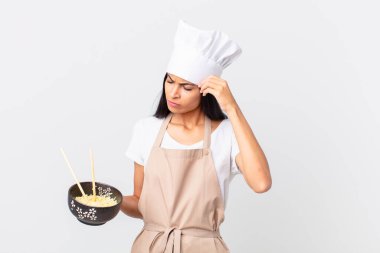 Güzel İspanyol aşçı kadın şaşkın ve kafası karışmış hissediyor. Kafasını kaşıyor ve elinde erişte kasesi tutuyor.
