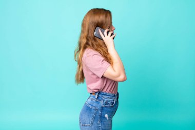 Profil görüntüsünde kızıl saçlı güzel bir kadın hayal kuruyor, hayal kuruyor ve akıllı telefon kullanıyor.