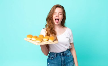 Kızıl saçlı, güzel, neşeli ve asi tavırlı bir kadın, şaka yapıyor, dilini dışarı çıkarıyor ve ekmekli çörek tutuyor.