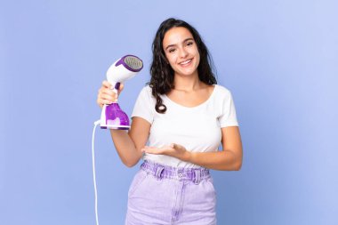 İspanyol güzel kadın neşeyle gülümsüyor, mutlu hissediyor ve bir konsept gösteriyor ve demir buhar tutuyor.