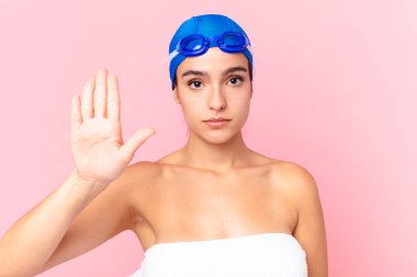 İspanyol güzel yüzücü kadın ciddi görünüyor. Avuç içini gösteriyor. Gözlüklü jesti durduruyor.