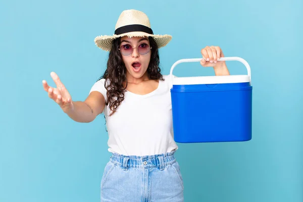 Pretty Hispanic Woman Feeling Extremely Shocked Surprised Holding Portable Refrigerator — Stock Photo, Image