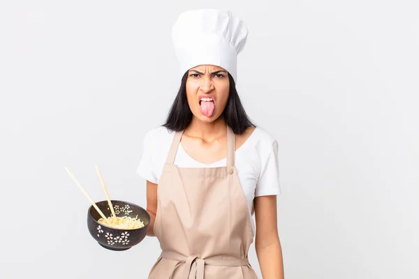 pretty hispanic chef woman feeling disgusted and irritated and tongue out and holding a noodle bowl