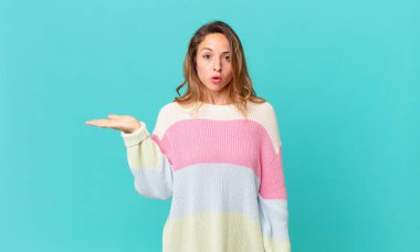 Güzel bir kadın şaşırmış ve şok olmuş görünüyor, çenesi düşmüş bir nesne tutuyor.