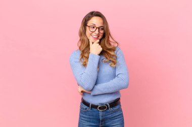 Güzel bir kadın mutlu, kendinden emin bir ifadeyle gülümsüyor, elleri çenesinde.