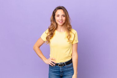 Güzel kadın mutlu bir şekilde gülümsüyor, eli kalçasında ve kendinden emin.