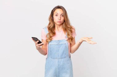 Güzel bir kadın şaşkın, şaşkın, şüpheci ve elinde bir akıllı telefon tutuyor.