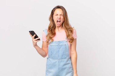 Güzel bir kadın agresif bir şekilde bağırıyor, çok kızgın görünüyor ve elinde bir akıllı telefon tutuyor.