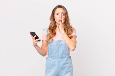 Güzel bir kadın şok olmuş, korkmuş ve elinde akıllı bir telefon tutuyor.