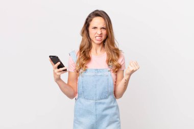 Güzel bir kadın kızgın bir ifadeyle agresif bir şekilde bağırıyor ve elinde bir akıllı telefon tutuyor.