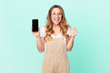 Güzel bir kadın şok geçiriyor, gülüyor, başarıyı kutluyor ve elinde bir akıllı telefon tutuyor.