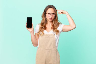 Güzel bir kadın kafası karışık ve şaşkın hissediyor, deli olduğunu ve elinde akıllı telefon tuttuğunu gösteriyor.