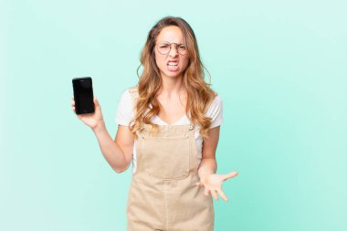 Güzel bir kadın sinirli, sinirli ve hayal kırıklığına uğramış görünüyor ve elinde bir akıllı telefon tutuyor.