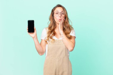 Güzel bir kadın şok olmuş, korkmuş ve elinde akıllı bir telefon tutuyor.