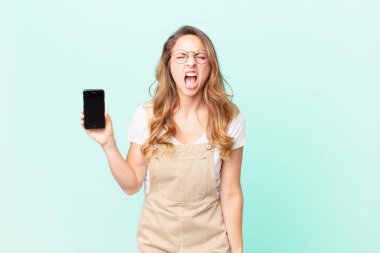 Güzel bir kadın agresif bir şekilde bağırıyor, çok kızgın görünüyor ve elinde bir akıllı telefon tutuyor.
