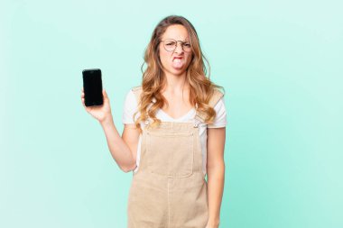 Güzel bir kadın midesi bulanmış ve rahatsız olmuş hissediyor ve dilini çıkarıp akıllı bir telefon tutuyor.