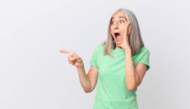 Orta yaşlı, beyaz saçlı, mutlu, heyecanlı ve şaşırmış bir kadın.