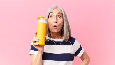 Orta yaşlı beyaz saçlı kadın elinde kahve termosu tutuyor.