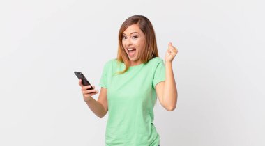 Güzel bir kadın şok geçiriyor, gülüyor, başarıyı kutluyor ve akıllı telefon kullanıyor.