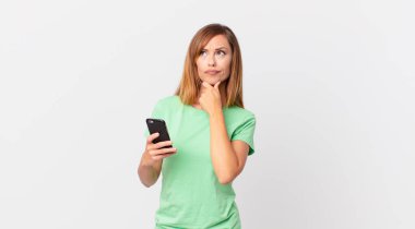 Güzel bir kadın düşünüyor, kuşkulu hissediyor ve kafası karışık ve akıllı telefon kullanıyor.