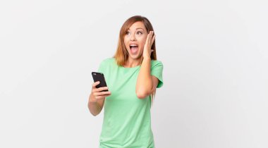 Güzel bir kadın mutlu, heyecanlı ve şaşırmış ve akıllı telefon kullanıyor.