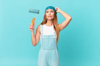 Güzel kadın şaşkın ve kafası karışmış hissediyor, yeni bir ev duvarı boyuyor.