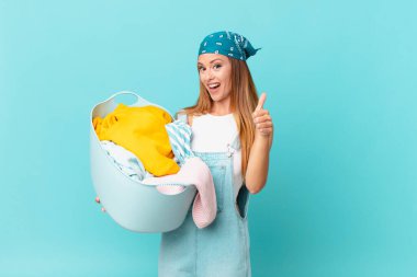 Güzel bir kadın gururlu, olumlu gülümsüyor, parmakları havada, çamaşır sepetini tutuyor.