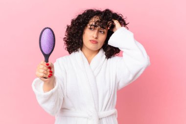 Bornoz giyen ve elinde saç fırçası tutan güzel bir Arap kadın.