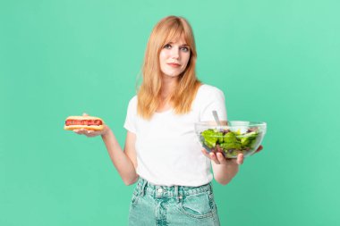 Güzel kızıl saçlı kadın elinde salata ve sosisli sandviç tutuyor. diyet kavramı