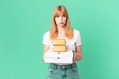 Güzel kızıl saçlı kadın elinde fast food paketleri tutuyor.