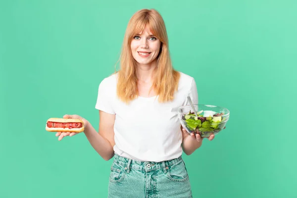 漂亮的红头发女人拿着沙拉和热狗 饮食概念 — 图库照片
