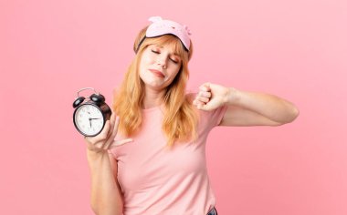 Pijama giyen ve elinde çalar saat tutan güzel kızıl saçlı kadın. Uyan konsepti