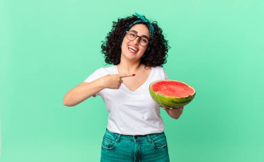 Güzel bir Arap kadın heyecanlı ve şaşırmış görünüyor. Yan tarafı gösterip elinde bir karpuz tutuyor. yaz konsepti