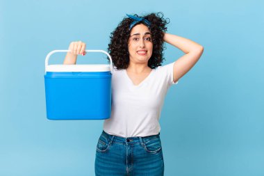 Güzel Arap kadın stresli, endişeli ya da korkmuş hissediyor, elleri başının üstünde ve portatif bir buzdolabı tutuyor.