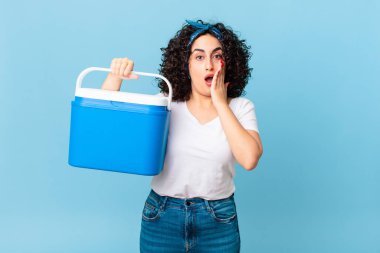 Güzel Arap kadın şok olmuş ve korkmuş hissediyor ve portatif bir buzdolabı tutuyor.