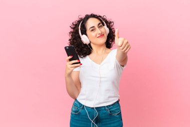 Güzel Arap kadın gururlu, olumlu gülümsüyor. Kulaklığı ve akıllı telefonu var.