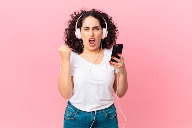 Güzel Arap kadın sinirli bir ifadeyle, kulaklıkla ve akıllı telefonuyla saldırganca bağırıyor.