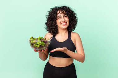 Güzel Arap kadın neşeyle gülümsüyor, mutlu hissediyor ve bir konsept gösteriyor ve salata tutuyor. diyet kavramı