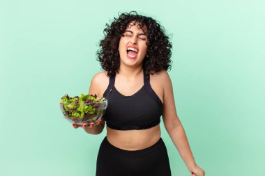 Güzel Arap kadın saldırganca bağırıyor, çok kızgın görünüyor ve elinde salata tutuyor. diyet kavramı
