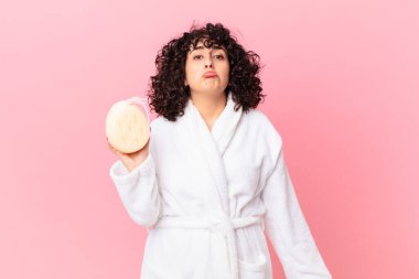 Güzel bir Arap kadın üzgün ve mızmız görünüyor. Mutsuz görünüyor ve ağlıyor. Bornoz giyiyor ve sünger tutuyor.