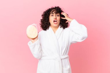 Güzel Arap kadın ellerini havaya kaldırıp bağırıyor bornoz giyiyor ve sünger tutuyor.