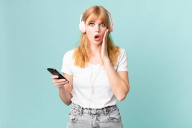 Güzel kızıl saçlı kadın şok olmuş ve korkmuş hissediyor ve kulaklıkla müzik dinliyor.