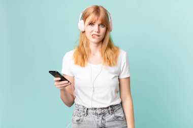 Güzel kızıl saçlı kadın kafası karışmış görünüyor ve kulaklıkla müzik dinliyor.